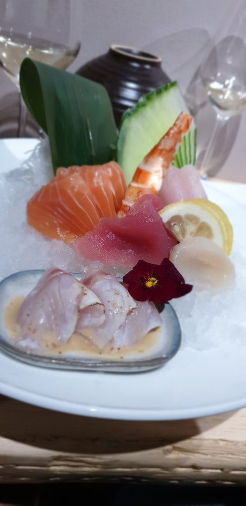 Piatto di sashimi con salmone, tonno, ricciola e gambero su ghiaccio tritato.