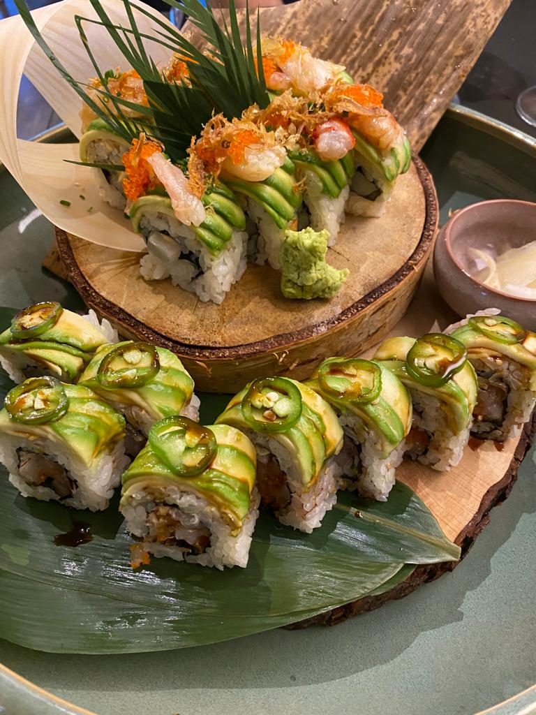 Uramaki coperti da fette di avocado e rondelle di jalapeño, serviti su una foglia verde.