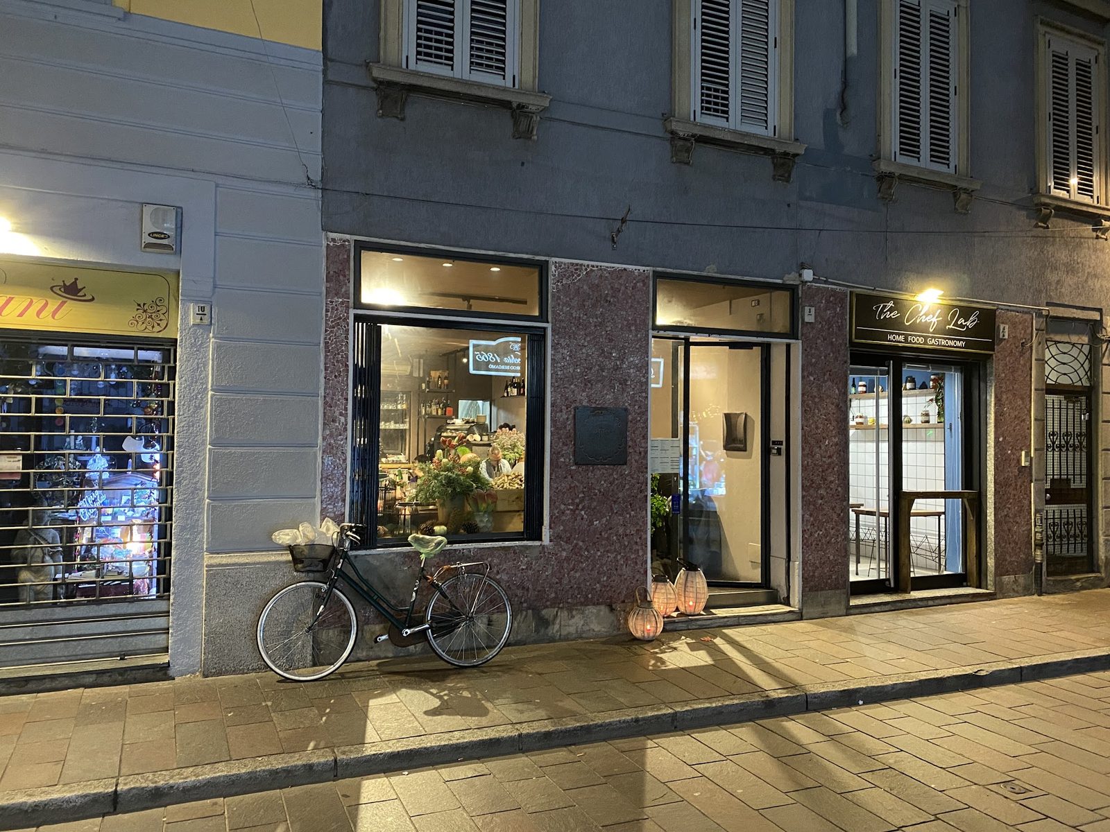 Via Bergamo di sera, con le vetrine illuminate e una bicicletta appoggiata al muro.